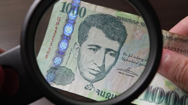 Examination of 1000 Armenian Dram cash money with magnfication glass, loupe. Concept of authenticity check, fight against counterfeiting of banknotes, anti fraud measures in Armenia. Close up view.