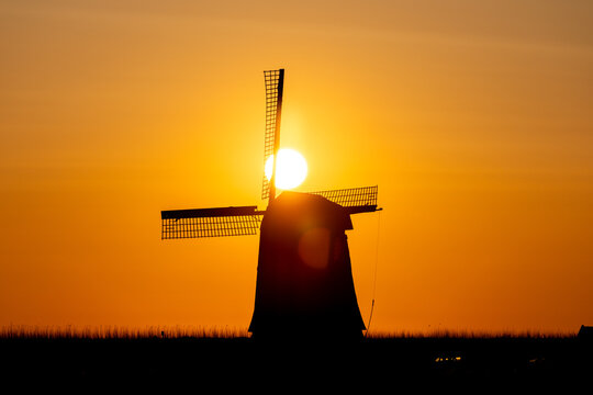 View of a traditional Dutch windmill silhouette against a vibrant orange sunset sky Schermerhorn, North Holland, Netherlands.