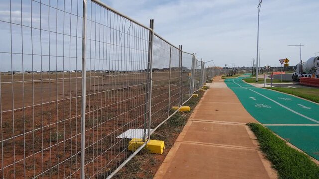 a row of temporary construction fencing&nbsp;bordering a large undeveloped land parcel in a new Australian residential estate in Tarneit, Melbourne, Australia.&nbsp;Early-stage estate infrastructure