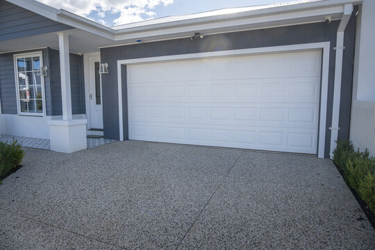 A neat double garage with a white panel lift door and&nbsp;exposed aggregate concrete driveway on a contemporary single-storey Australian home. Modern Australian residential design and curb appeal