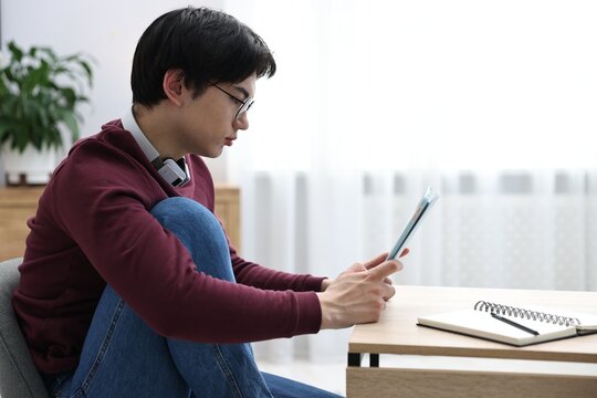 Young student studying with tablet at wooden table indoors