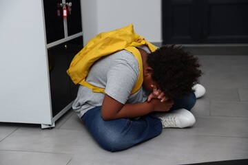 Bullying. Upset boy with backpack sitting near lockers at school © New Africa