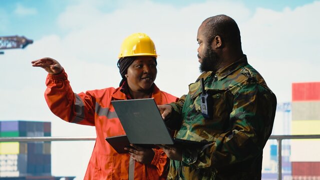 Military personnel stationed on offshore rig analyzing tactical data on laptop. Soldier provides protection to drilling barge, reviewing mission dashboard on notebook