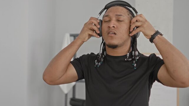 Man adjusting headphones and listening while training with braided hair and beads in a workout studio; determination.