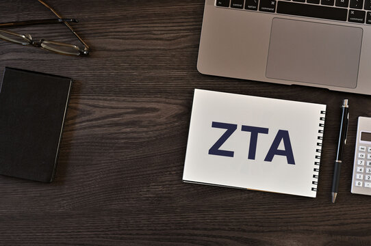 Eye-catching image of ZTA text on notebook. The word stands for Zero Trust Architecture. Shown with laptop, calculator.
