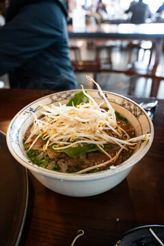 generous bowl of traditional Vietnamese Beef Pho served in a blue-and-white patterned ceramic bowl topped with generous amount of bean sprout and basil leaves