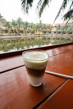 a Vietnamese coconut coffee, resting on a polished reddish-brown wooden table