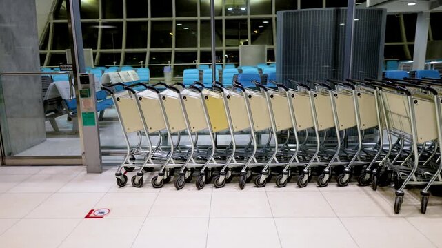 Row of metal luggage trolleys in empty airport terminal at night.