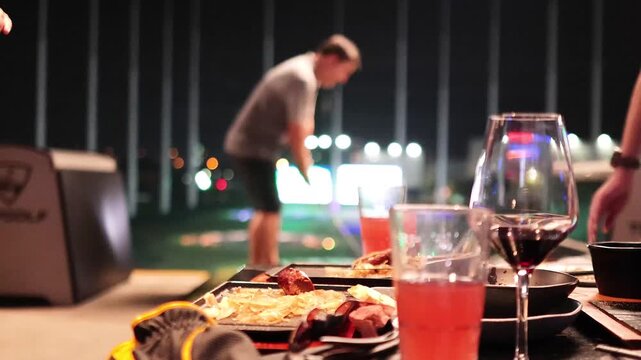 Group of friends playing indoor golf and celebrating at night with food and wine on table.