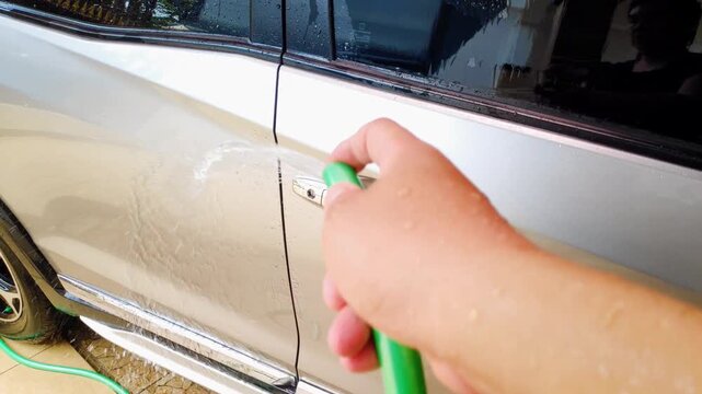 Man hand holding a hose pipe to wash a silver vehicle with slow motion water spray