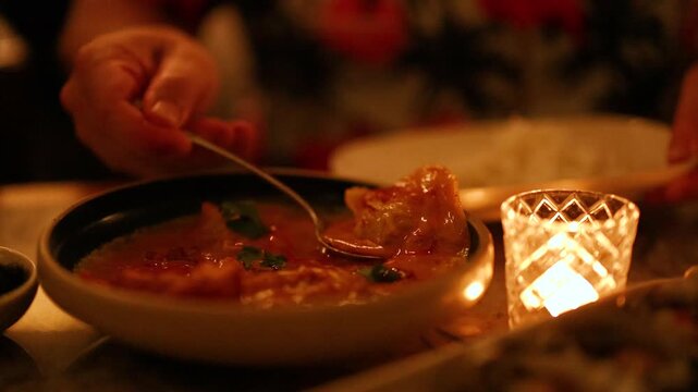 Serving hot spicy thai red curry with spoon in dim lit restaurant by candlelight.