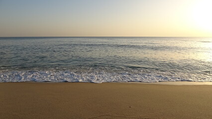 Fototapeta premium Peaceful Waves on a Sandy Beach at Early Mirning. Gentle white sea foam washing ashore on a clean sandy beach during early morning, featuring a soft gradient sky.