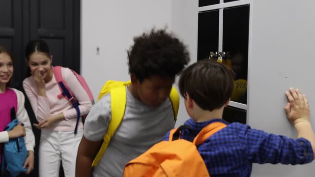Boy bullying his African American classmate near lockers in school hallway