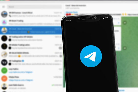 Cali, Colombia - June 12 2022: Smartphone displaying Telegram logo against a blurred background of the Telegram desktop application interface with various chat groups and contacts.