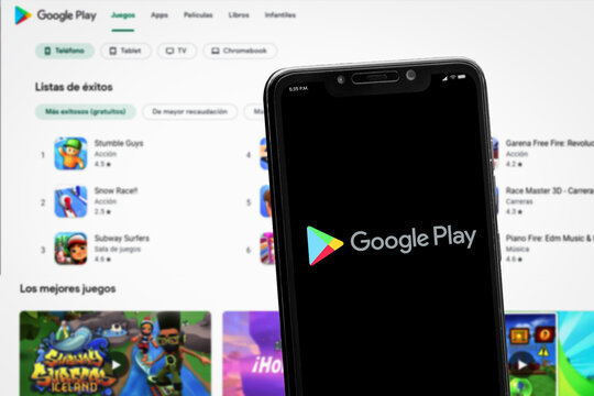 Cali, Colombia - June 12 2022: Smartphone displaying Google Play logo against a blurred background of the Google Play Store web interface showing various game apps.