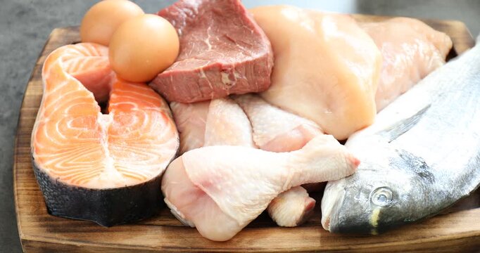Different types of fresh raw meat, fish and eggs on table, closeup. Camera zooming out