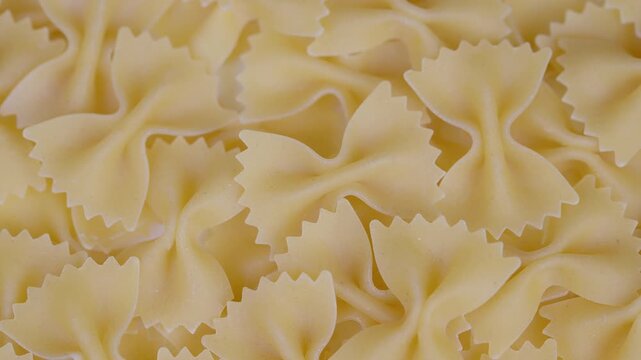 Closeup pile of bowshaped pasta, ridged edges and curled centers, pale beige tones, uncooked dry texture, overlapping farfalle filling frame for culinary background