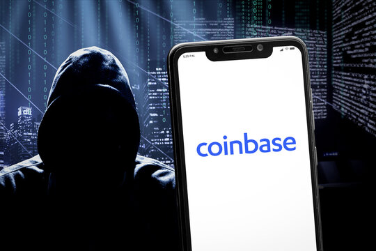 Cali, Colombia - April 20 2022: Smartphone displaying Coinbase logo against a blurred background featuring a hooded hacker silhouette and a dark cityscape with digital data patterns.