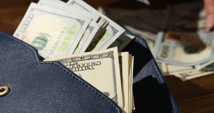 Woman counting money at wooden table, focus on wallet with old and new hundred dollar bills