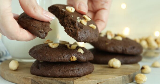 Woman breaking tasty chocolate cookie with hazelnuts at table, closeup