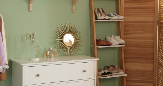 Rack with clothes, shoes on shelving unit and chest of drawers in hallway. Camera moving right