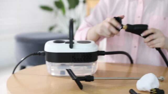 Woman assembling steam cleaner parts at wooden table indoors, closeup. Camera moving right