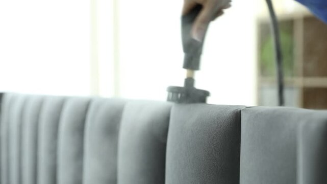 Woman cleaning bed headboard with steam cleaner at home, closeup
