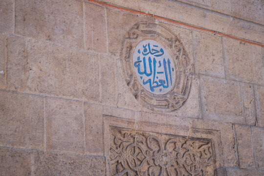 View of intricate blue Arabic calligraphy within a circular medallion on the historic stone walls of Al-Azhar Mosque, Cairo, Egypt.