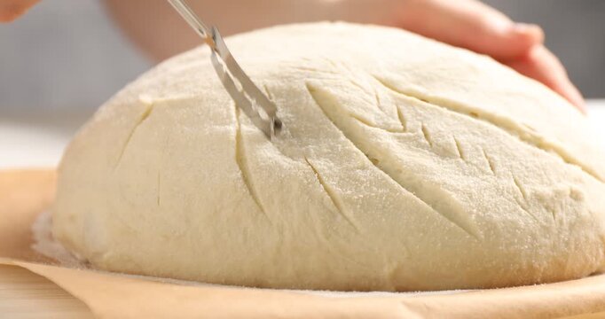 Woman scoring sourdough with lame at table, closeup