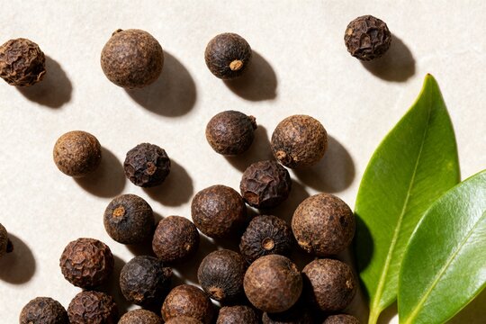 Assorted Dried Spices and Peppercorns Scattered on Light Surface with Green Leaves
