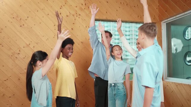 Caucasian teacher and happy diverse children putting hand together to celebrate successful project while standing circle. Represent love, corporate, team working, togetherness and unity. Edification