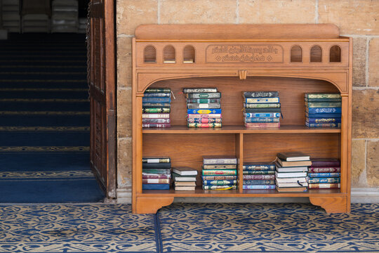 View of a wooden bookshelf filled with stacks of religious books on a blue patterned carpet at the Al-Azhar Mosque Cairo, Egypt.
