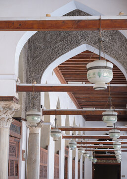 View of the Al-Azhar Mosque featuring intricate stucco carvings, hanging lanterns, and marble columns in Cairo, Egypt.