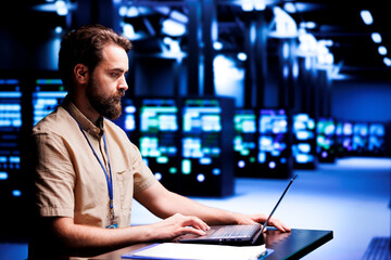 Fototapeta premium Computer scientist using laptop to patch up servers helping businesses manage databases, host websites and store files. Cloud computing business executive servicing supercomputers in data center