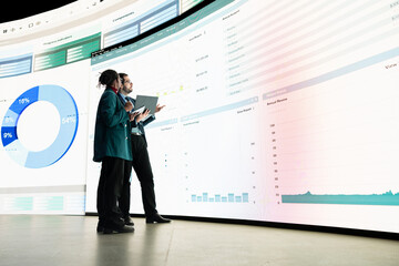 Calculating expenses, graph displayed on videowall and team of investors looking at projected...