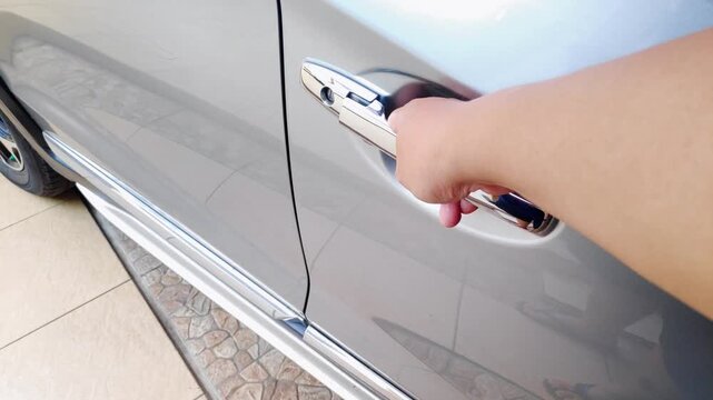Man hand opening a silver car door in slow motion using a shiny chrome handle