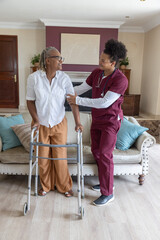 Caregiver with stethoscope helping Senior African American woman standing with walker at home