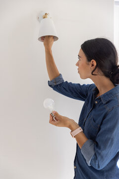 Conical white sconce is receiving clear incandescent bulb in hallway against smooth painted wall