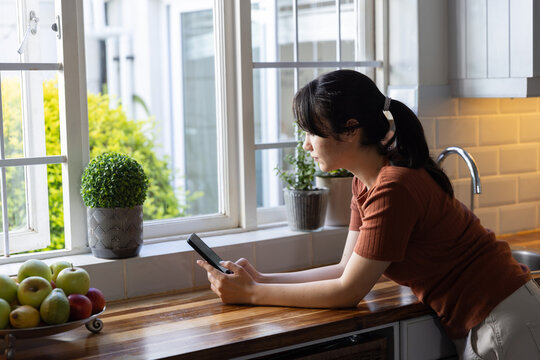 Smartphone resting on wooden countertop beside fruit bowl and potted plants by window, copy space