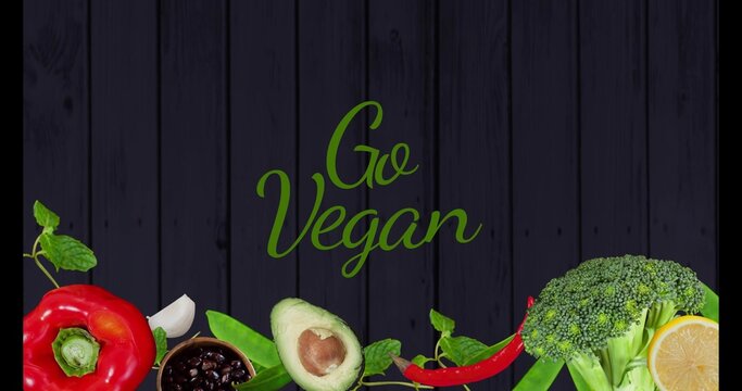Displaying green Go Vegan slogan centered on dark wooden planks, with halved red pepper and avocado