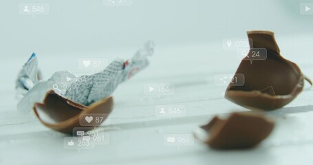 Displaying broken milk chocolate egg pieces resting on whitewashed table, with foil overlays © vectorfusionart