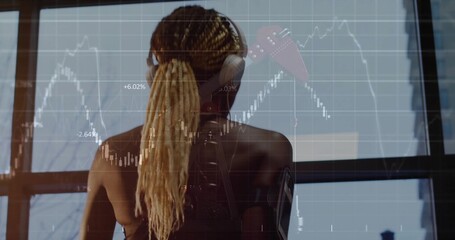 Obraz premium Standing woman with braids wearing tank and headset armband at home watching stock charts on window