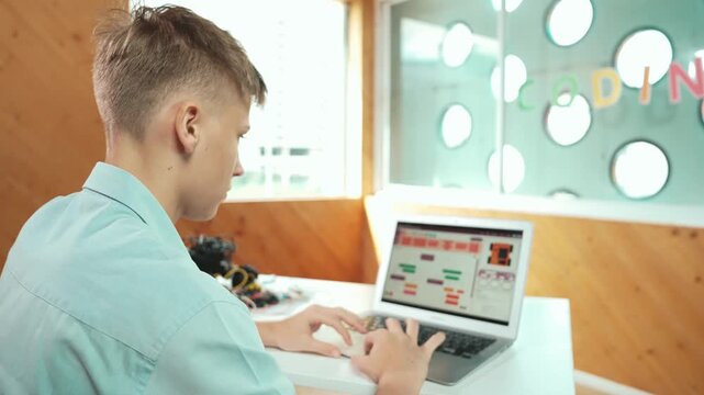 Back view of high school student working on laptop analysis data at STEM science class. Smart happy caucasian boy learning to coding engineering prompt or programming system at STEM class. Edification