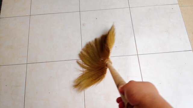 Man hand sweeping a tiled floor in slow motion with a traditional grass broom