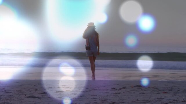 Woman walking to sea as dawn drawing her, holding camera, travel bokeh partially obscuring her