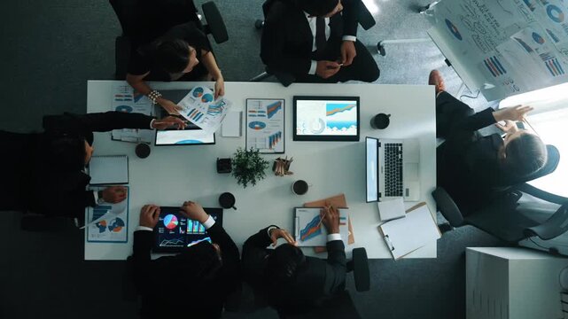 Top down aerial view of smart manager pointing at financial graph on whiteboard while diverse business team explain and plan marketing idea at meeting table with stock market statistic. Directorate.
