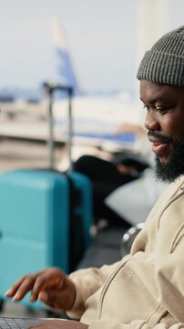 Vertical Video African american man on video conference call using airport internet, speaking to colleagues during online meeting while seated in the terminal waiting area. Digital communication and