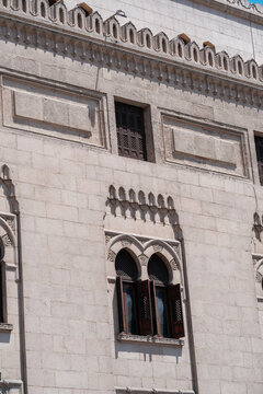 View of the historic stone facade and arched windows with wooden shutters of Al-Azhar Mosque in Cairo, Egypt.