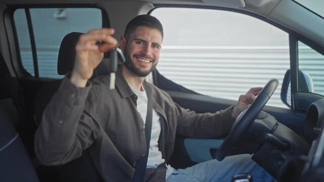 Man holding car keys and pointing hand toward camera while seated at steering wheel in street; confidence.