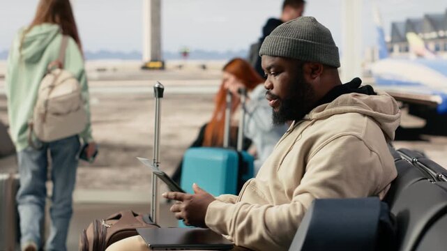 African american connected traveler in busy airport terminal lounge, typing on laptop and waiting for boarding flight. Modern digital nomad job and flexible career with travel lifestyle.